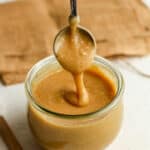 A tablespoon of caramel icing drizzling into a jar.
