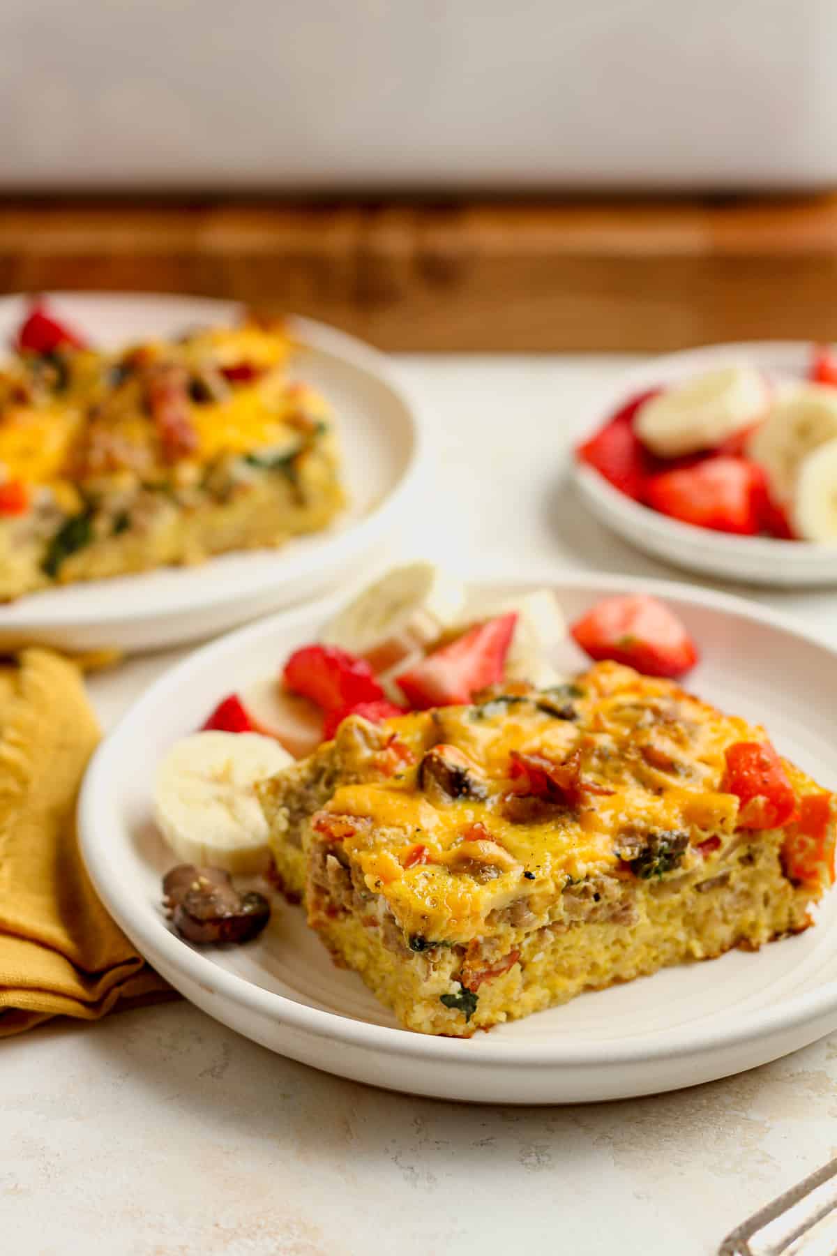 Two plates of overnight breakfast casserole with fruit.