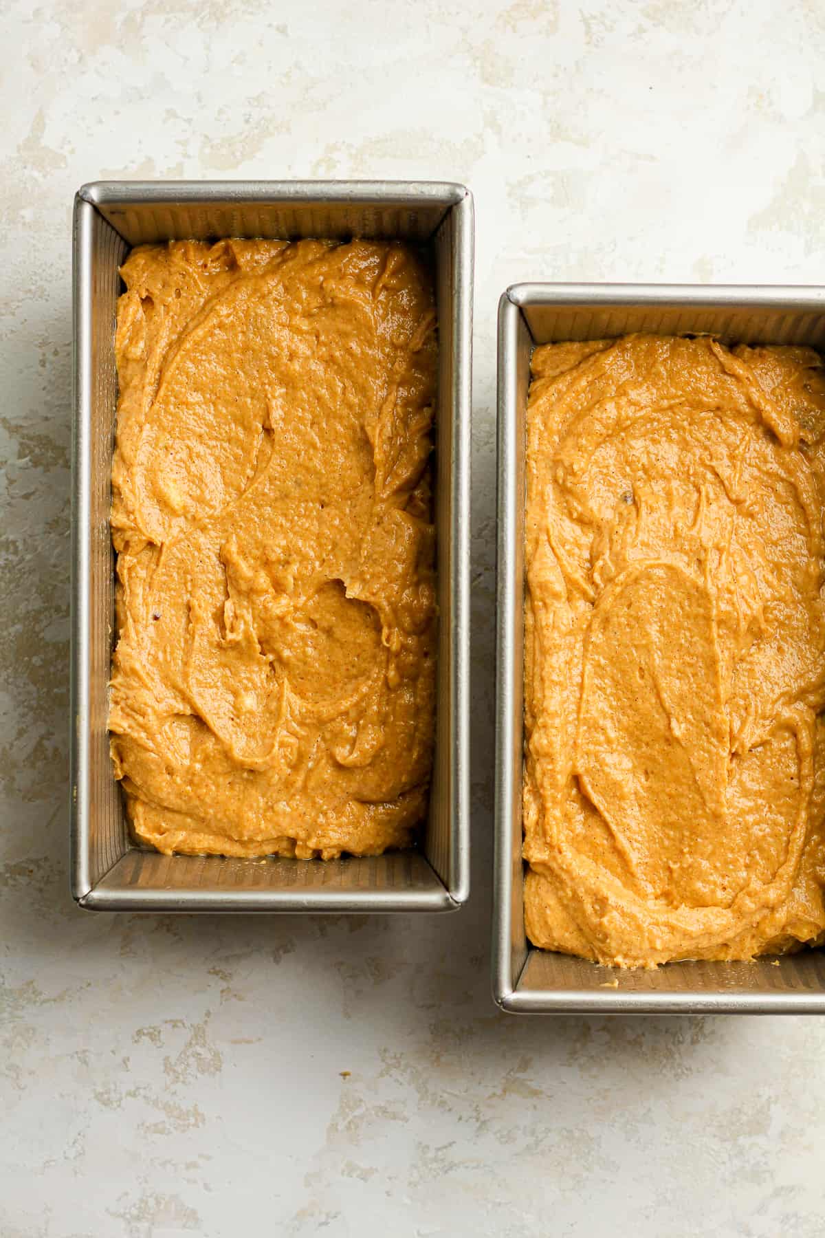 Overhead view of two loaves of pumpkin batter.