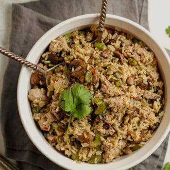 A round bowl of brown rice dressing with mushrooms and sausage.
