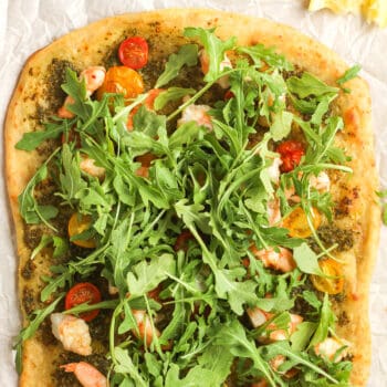 A just baked shrimp pesto flatbread with fresh arugula on top.