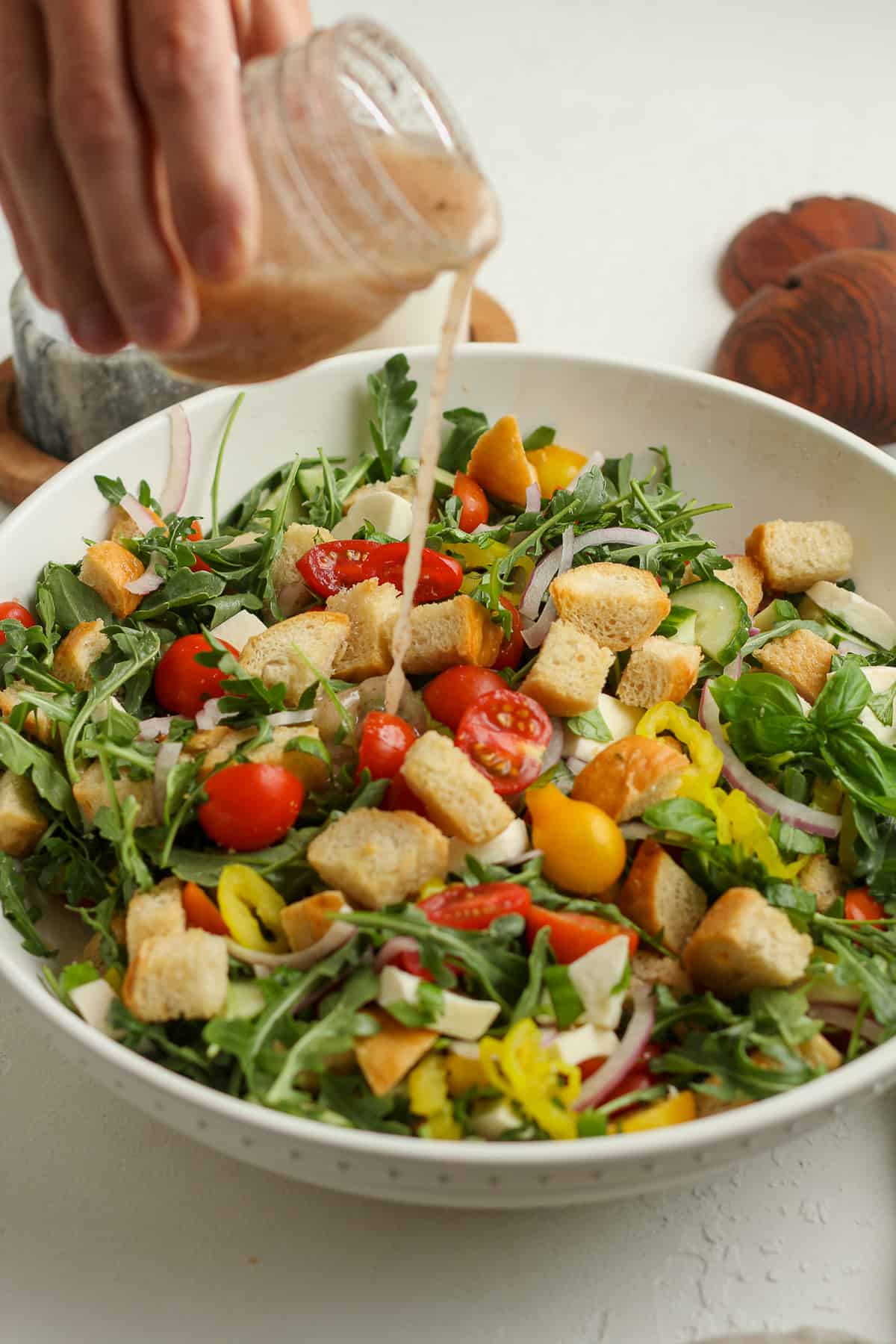 A hand drizzling dressing on a panzanella salad.