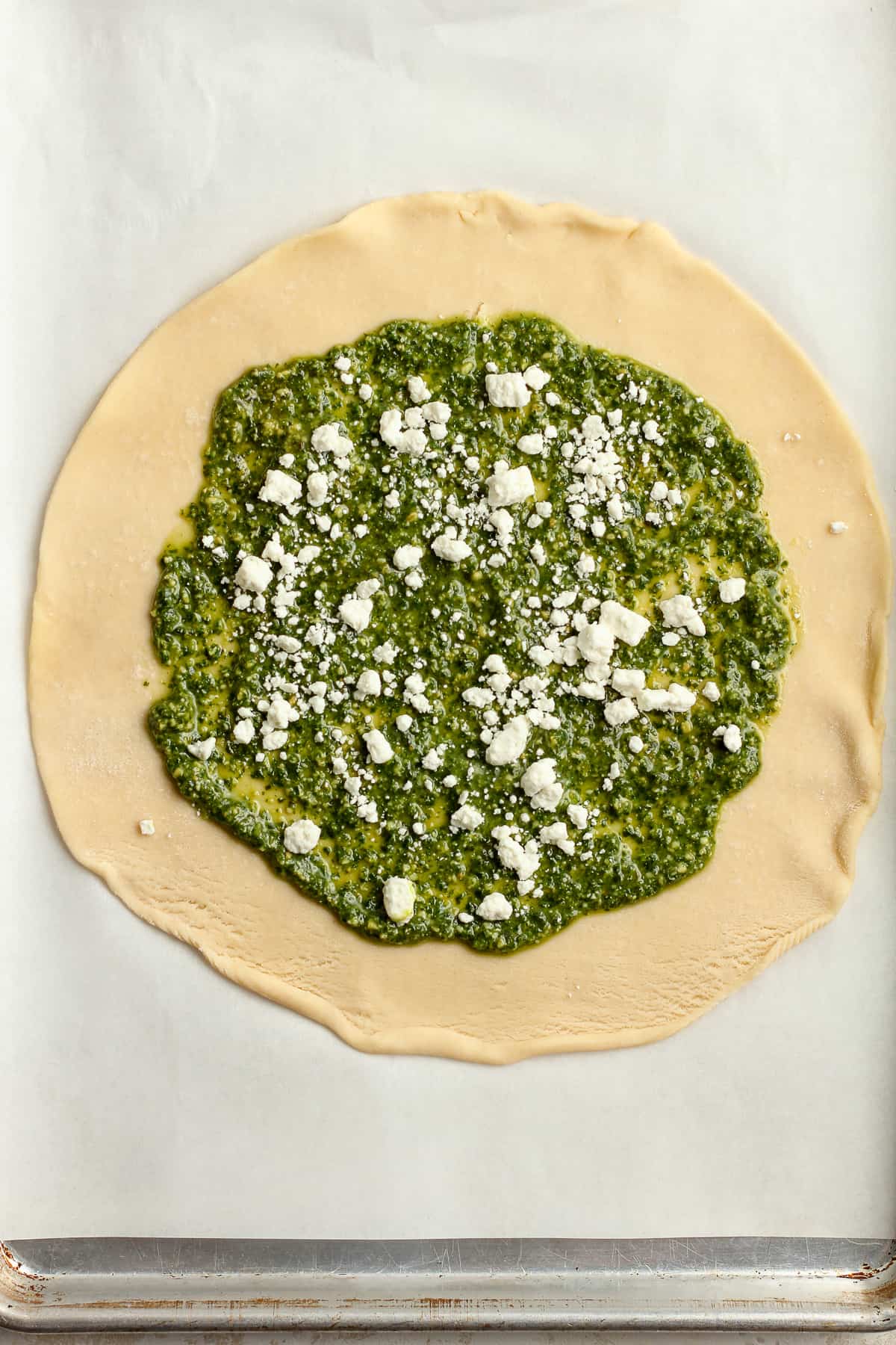A round pie crust with pesto sauce and some goat cheese.