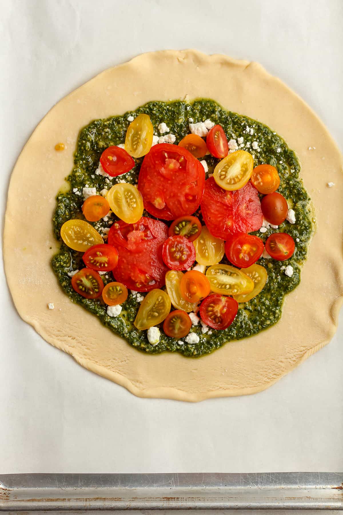 A pie crust with pesto sauce and tomatoes on top.