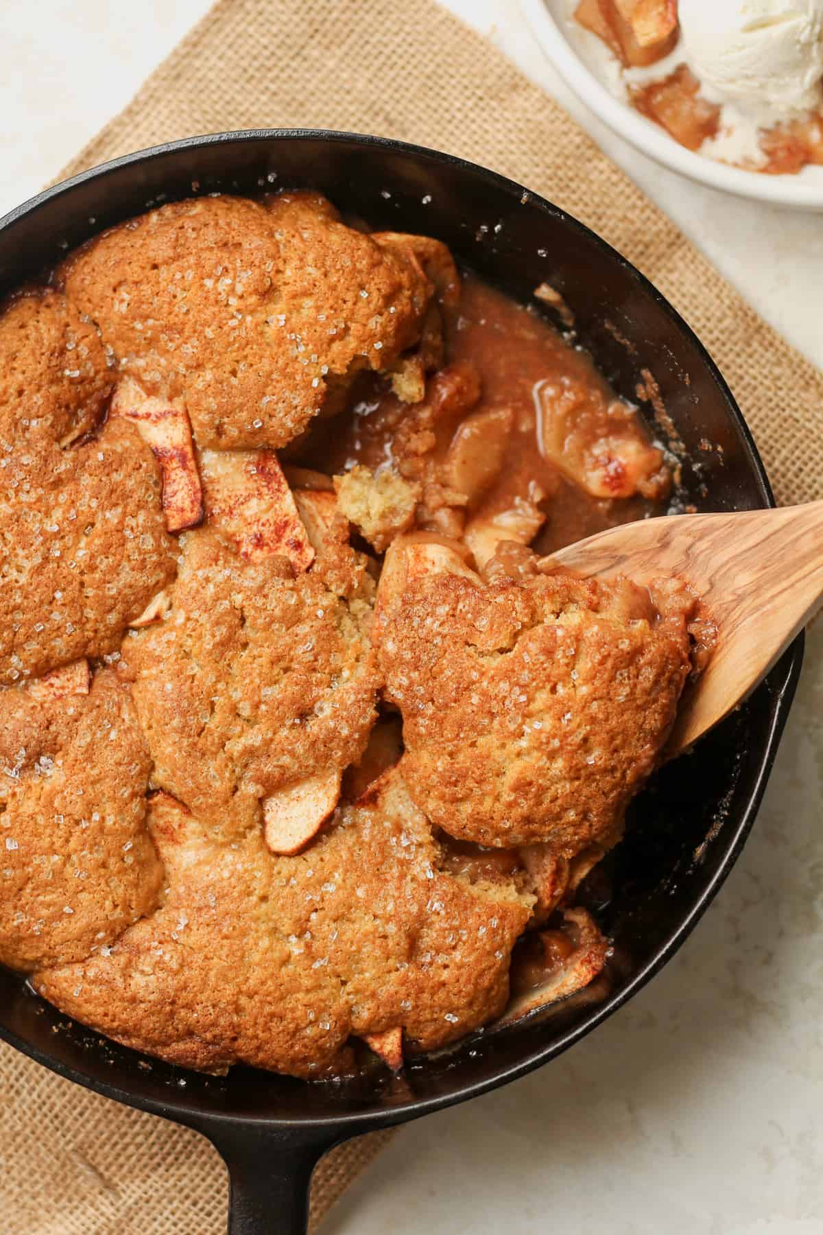 A cast iron skillet with the baked apple cinnamon cobbler with a spoonful.