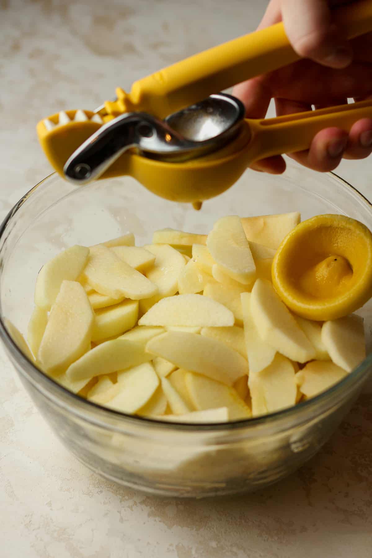 A bowl of the sliced apples with a citrus press squeezing a lemon over top.