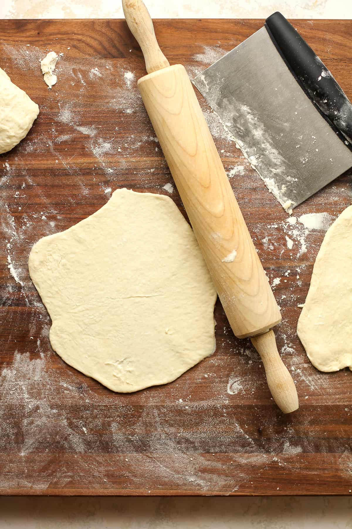 A board with a rolled out piece of naan with a rolling pin.