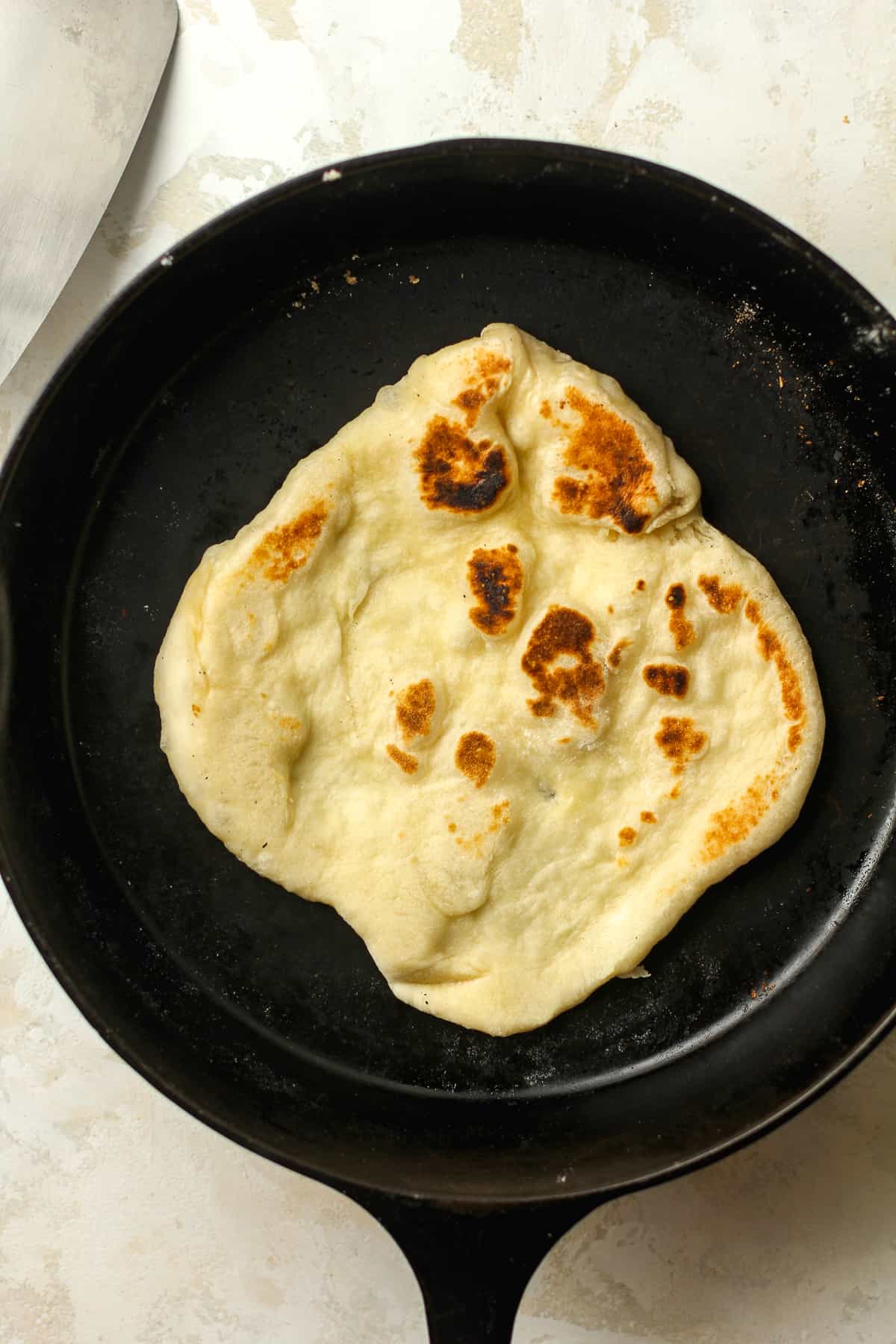 A cast iron with a piece of naan cooking.