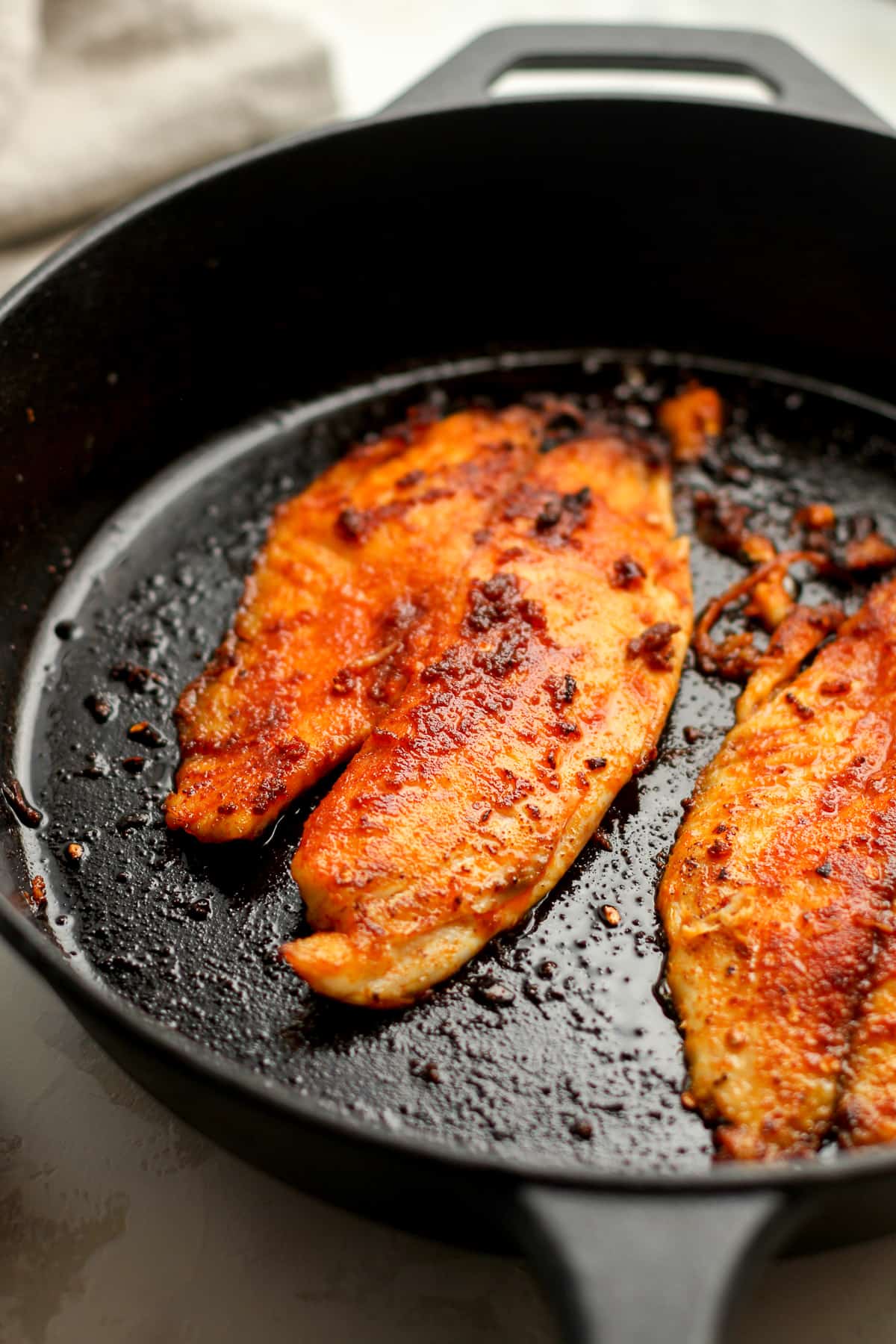 Side view of some blackened tilapia in a skillet.