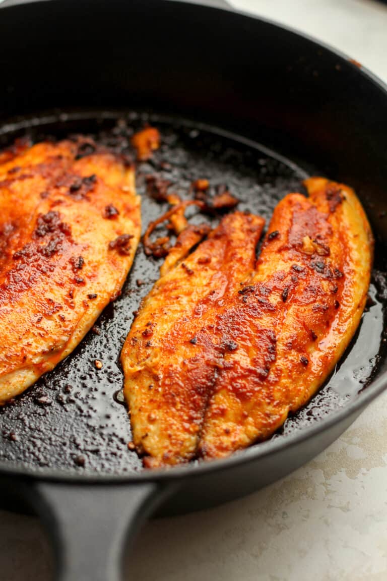 Side view of two pieces of blackened tilapia in a skillet.