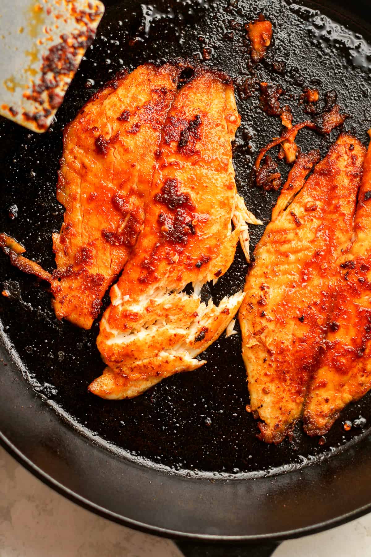 Closeup on some flaked tilapia in a cast iron skillet.