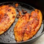 A cast iron with two pieces of blackened tilapia.