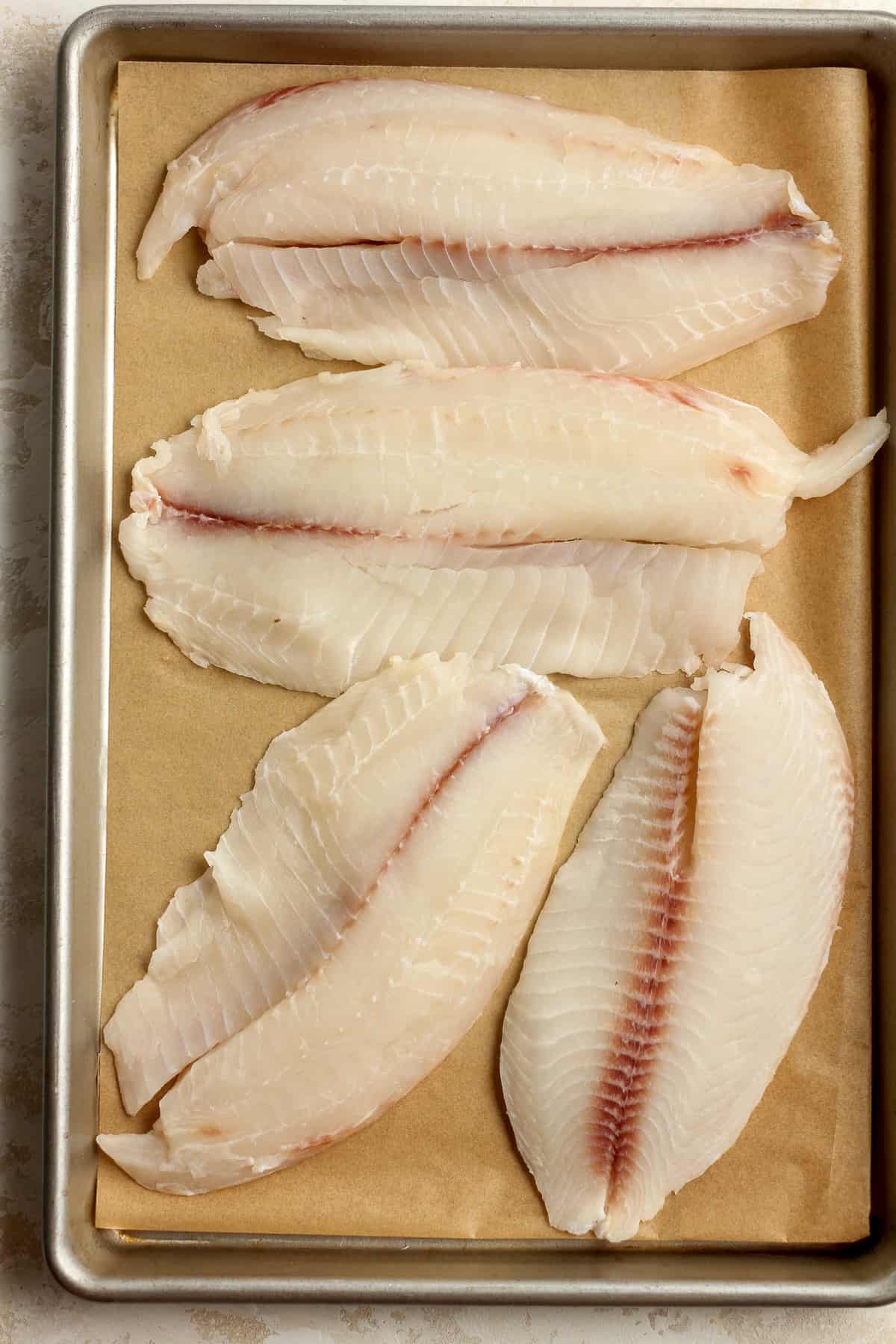 Four large pieces of raw tilapia on a pan.