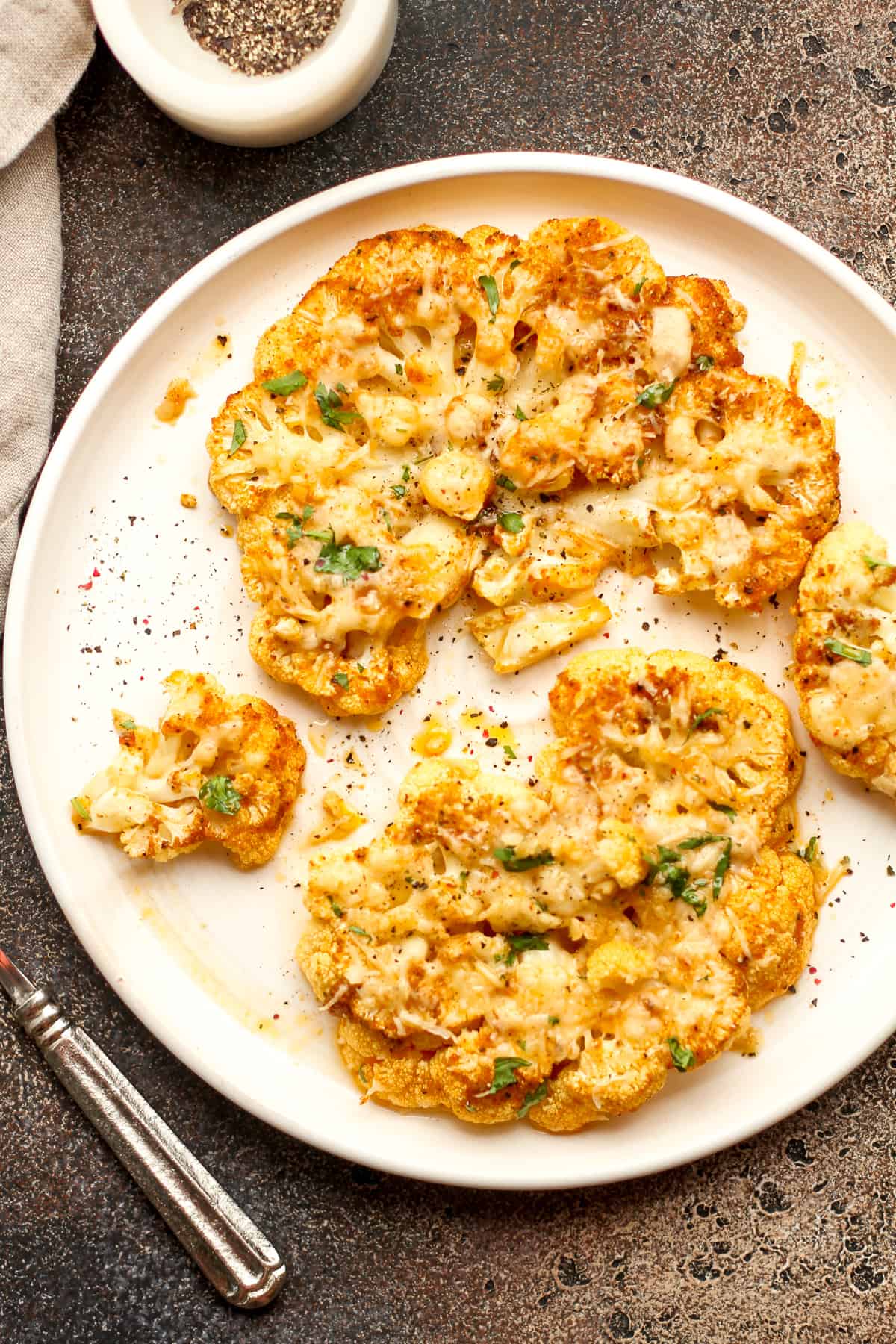 A white plate of two large cauliflower steaks with cheese.