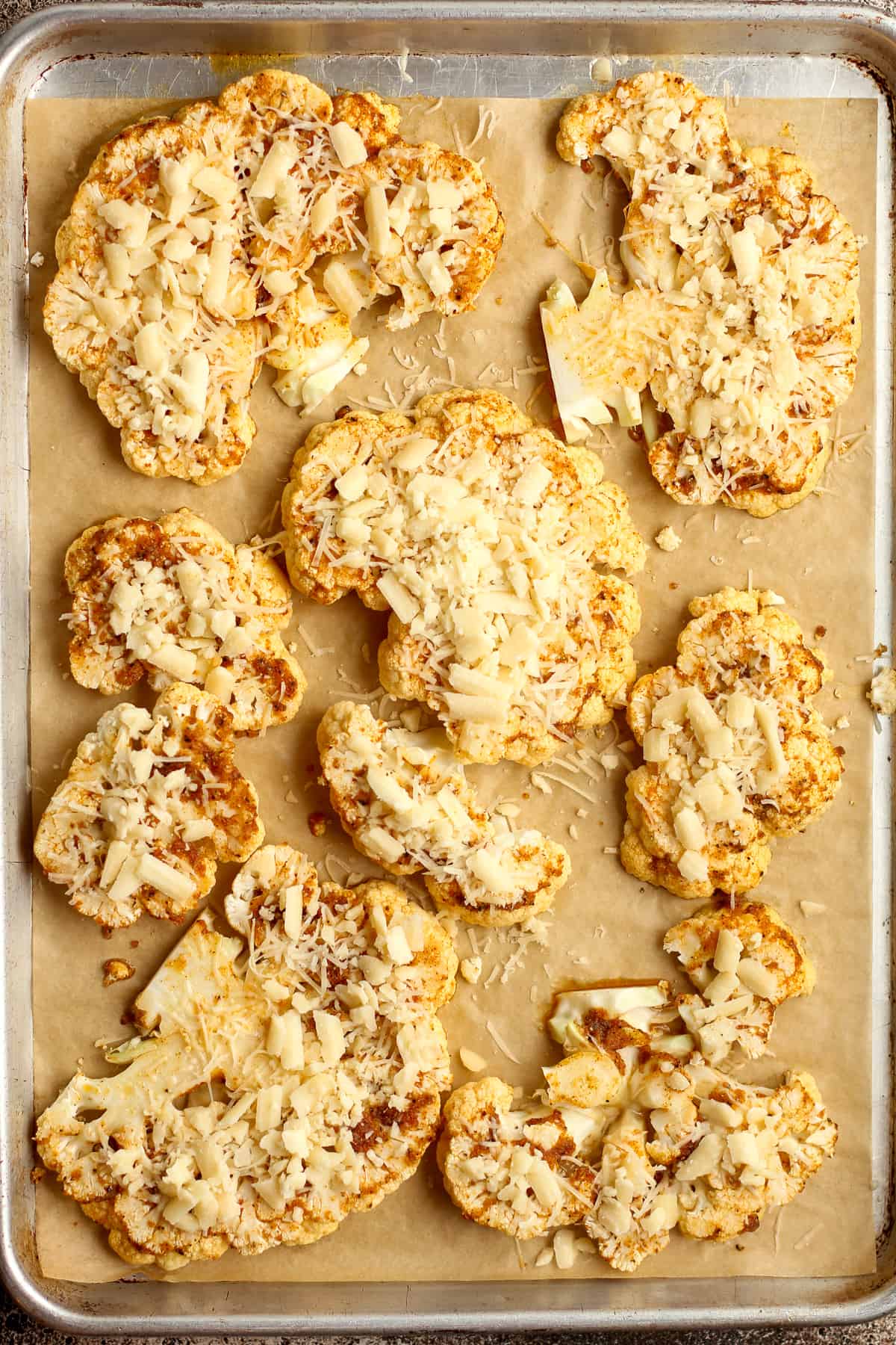 A pan of the cauliflower steaks with shredded cheese on top, before finishing the roasting.