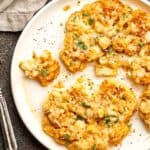A white plate of cheesy cauliflower steaks, with cilantro.