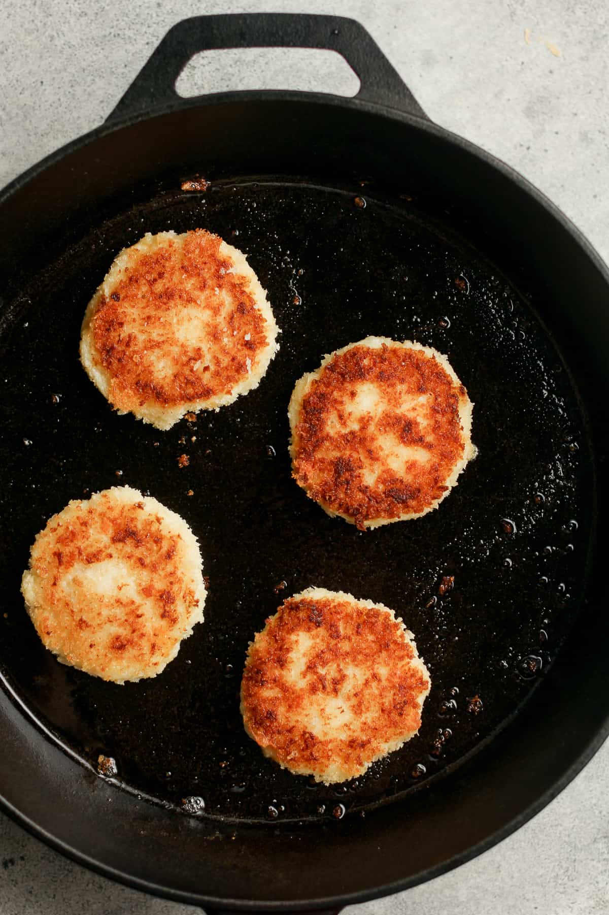 A cast iron skillet of potato cakes with cheese.
