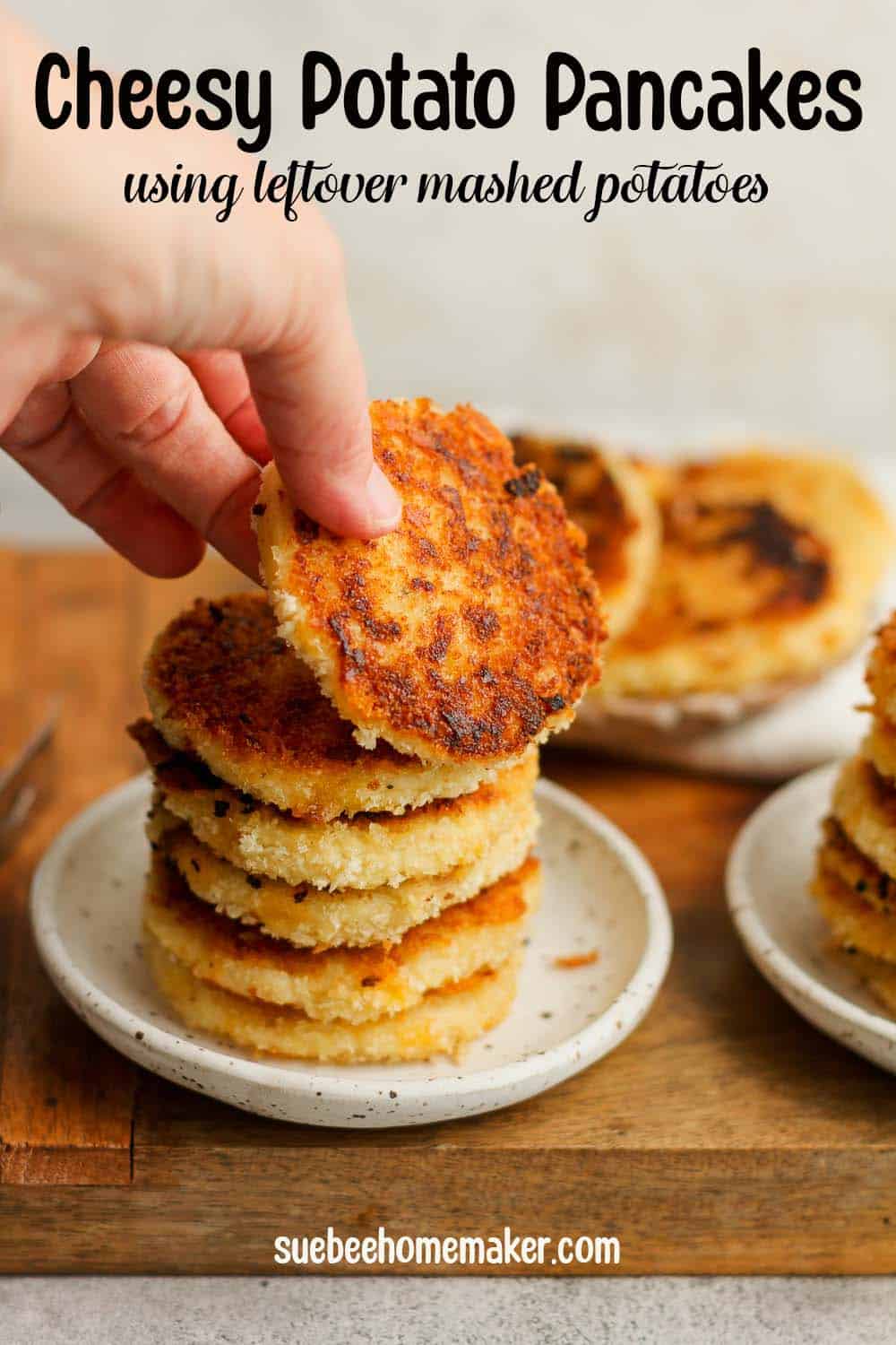 My hand reaching for a cheesy potato pancake from a stack of cakes.