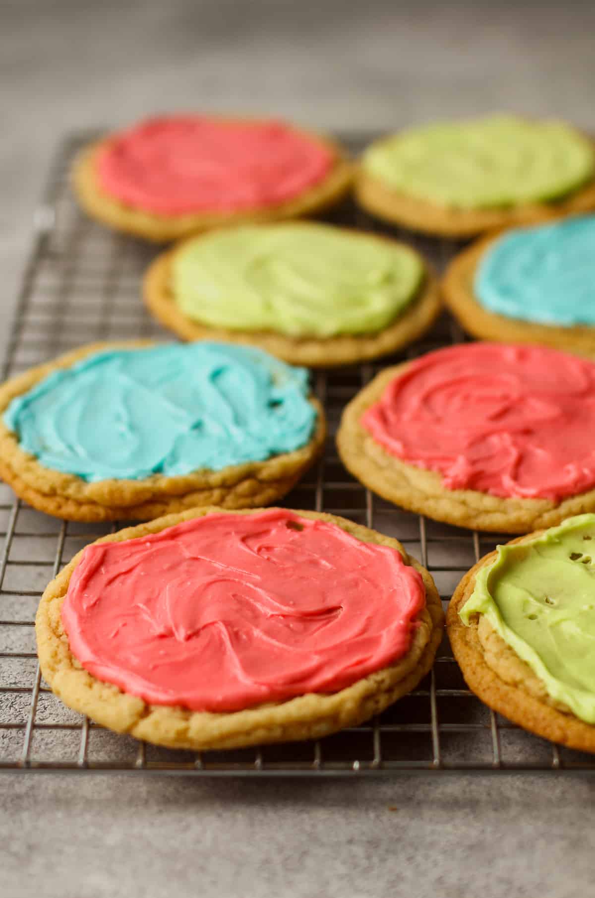 Side view of a cooling rack of frosted sugar cookies.