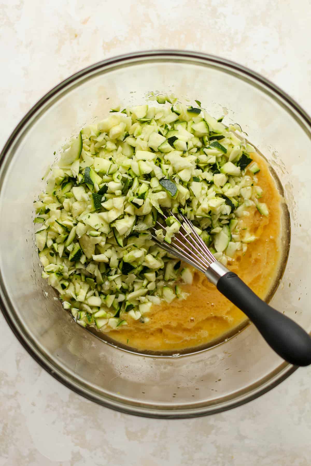 A bowl of the wet ingredients with the shredded zucchini on top.
