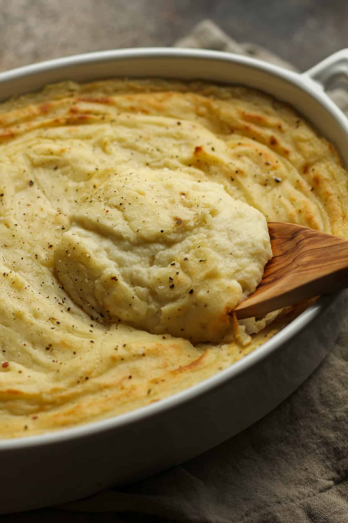 Side view of a scoop of creamy mashed potatoes over a casserole dish.