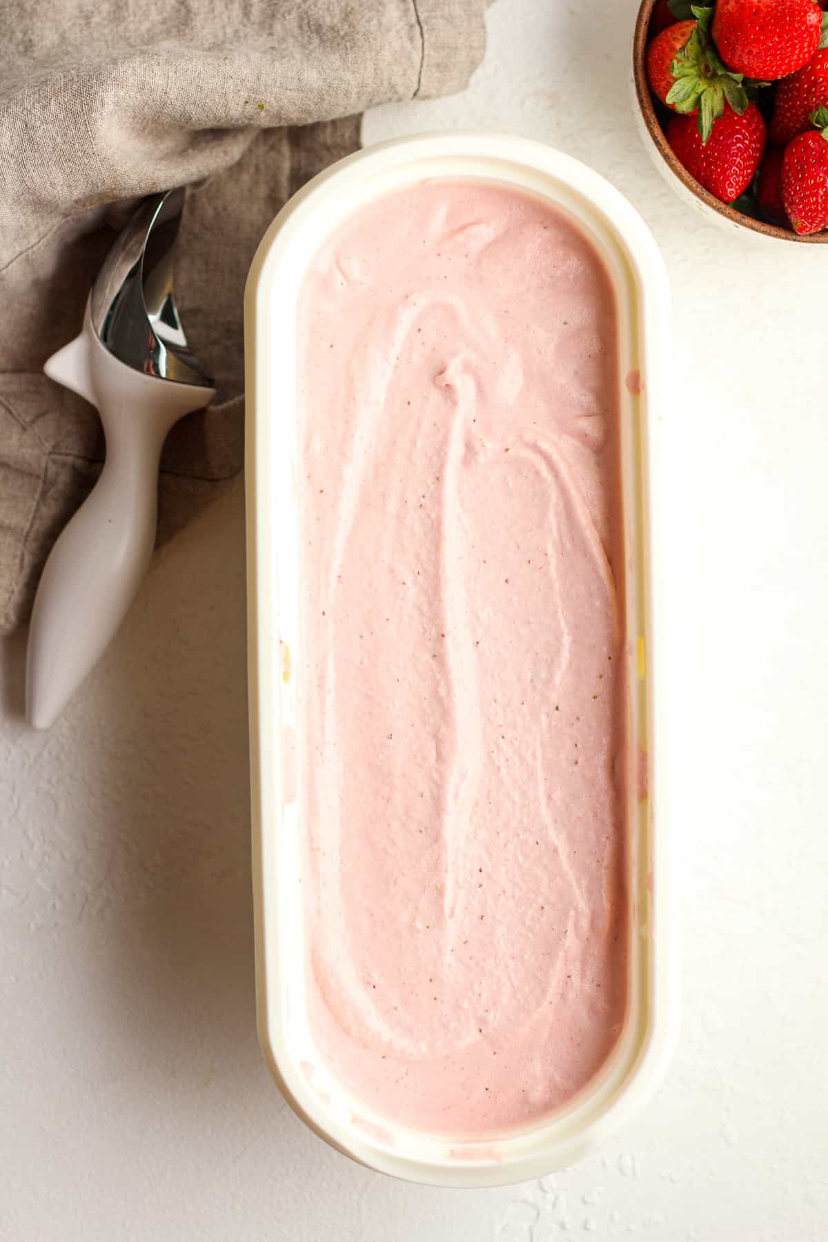 An oblong container of strawberry ice cream, with a bowl of strawberries.