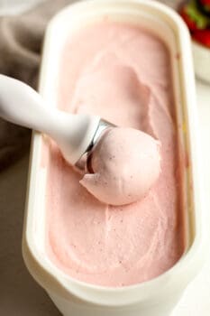 Side view of a container of strawberry ice cream scooping a scoop.