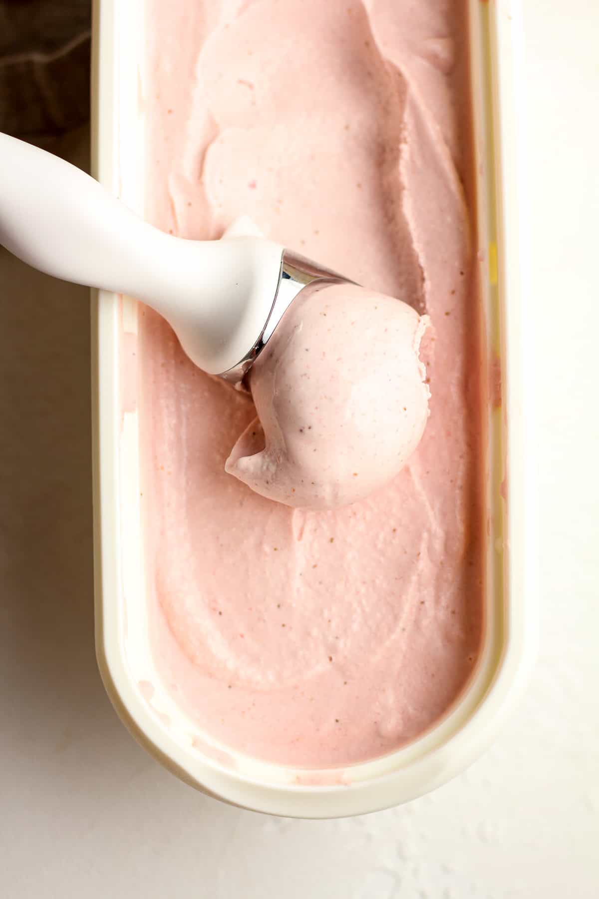 An ice cream scoop scooping up some strawberry ice cream.