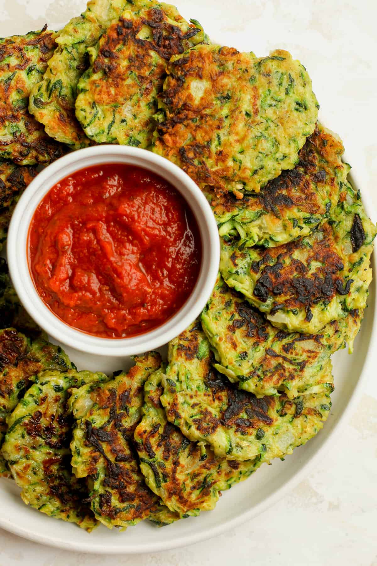 Overhead view of a plate of zucchini fritters and sauce.