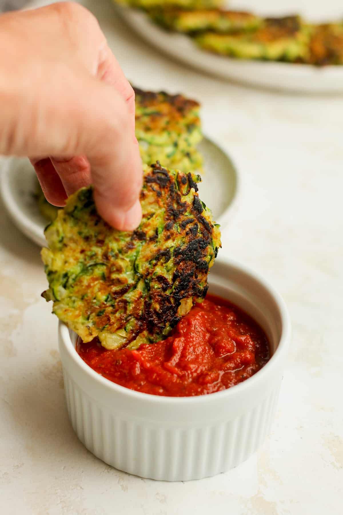 My hand dipping an Italian zucchini fritter in a bowl of sauce.