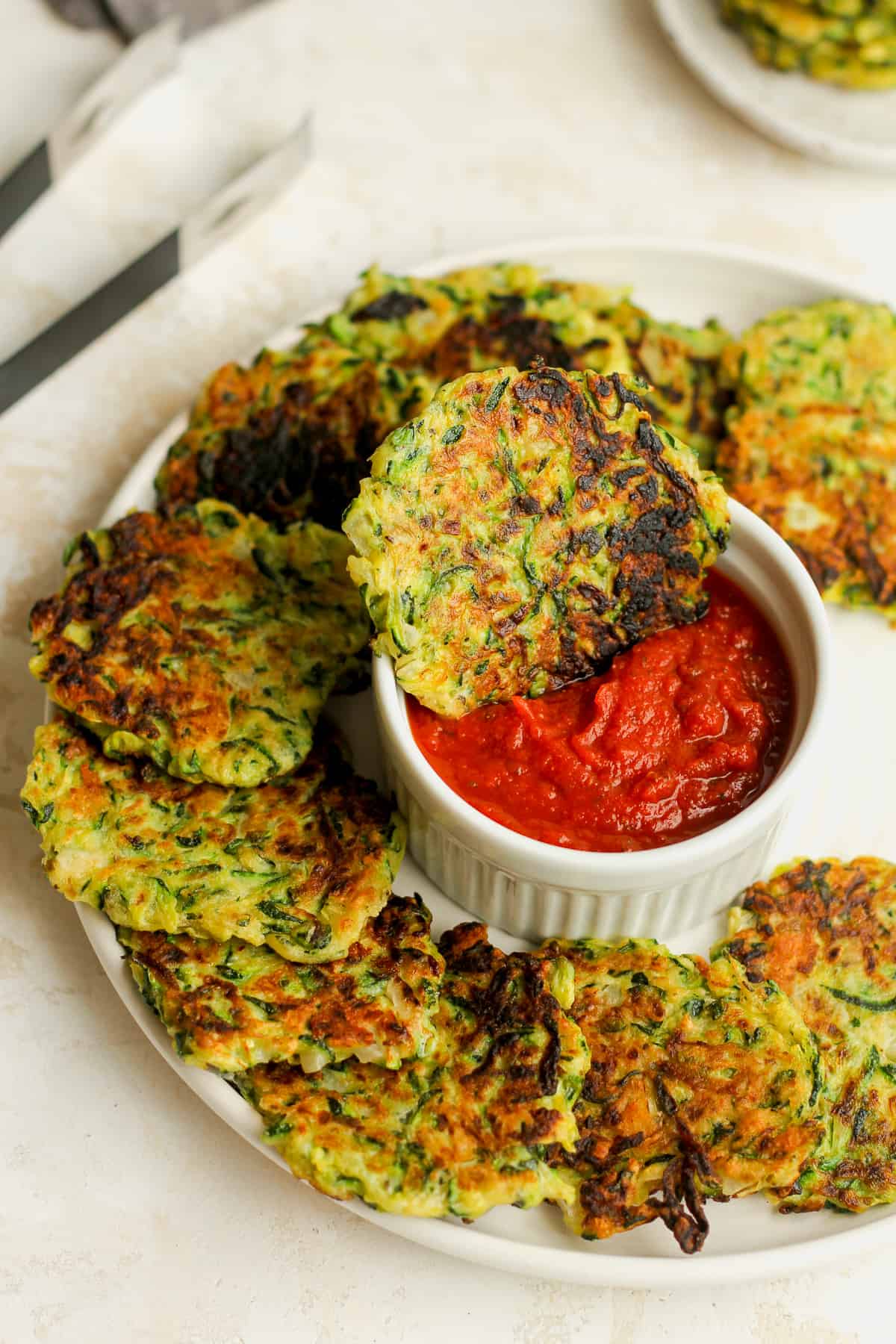 A plate of zucchini fritters with one fritter in a bowl of pizza sauce.