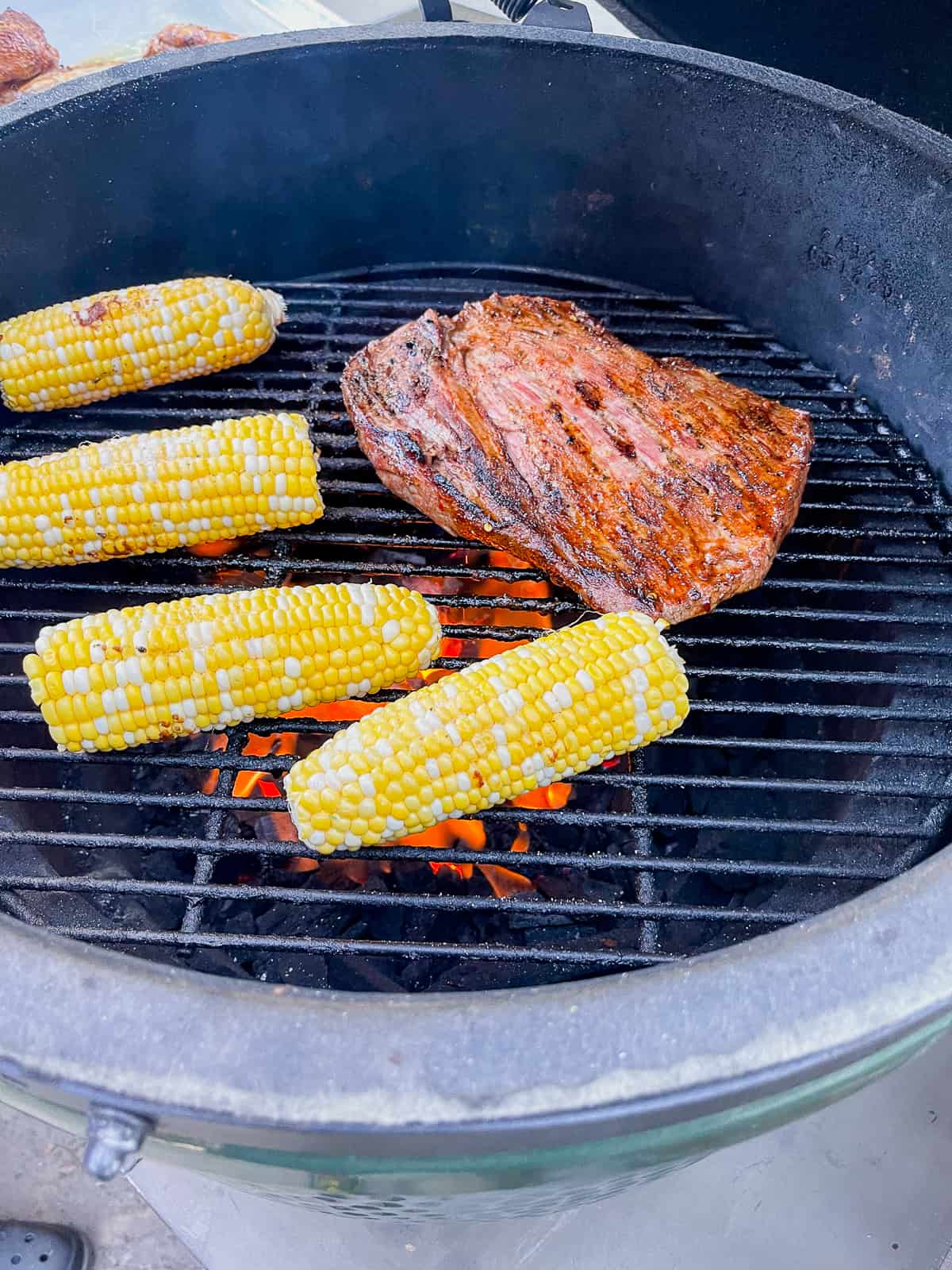 A big green egg with a flank steak and some ears of corn.