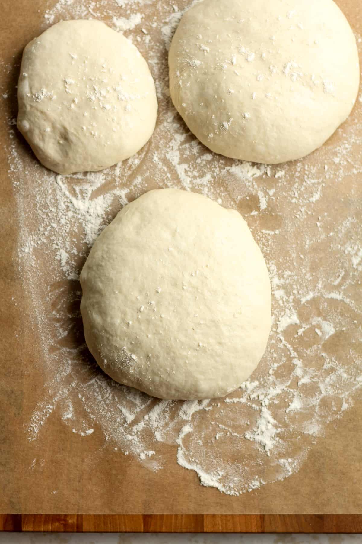Overhead shot of three mounds of pizza dough with flour.
