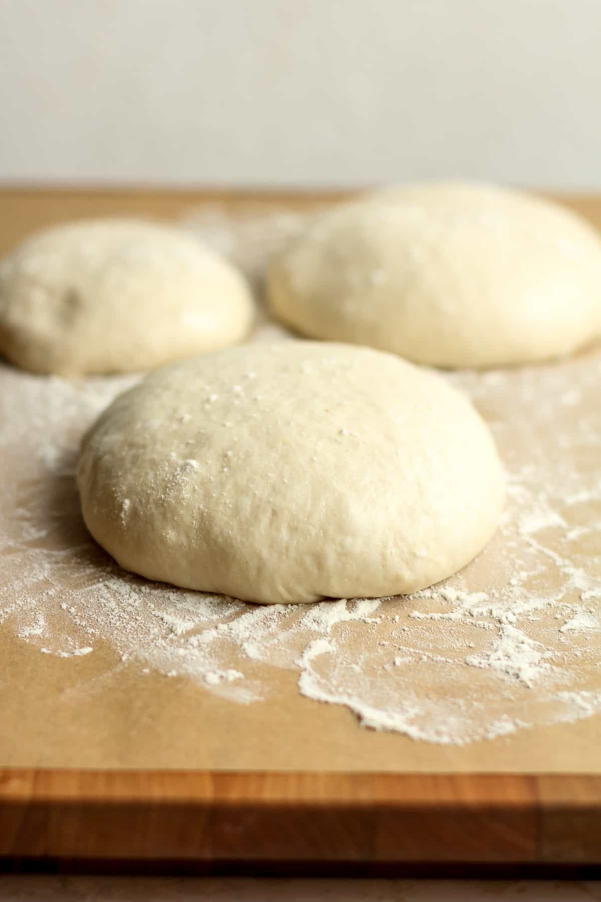 Side view of three mounds of pizza dough on a board.