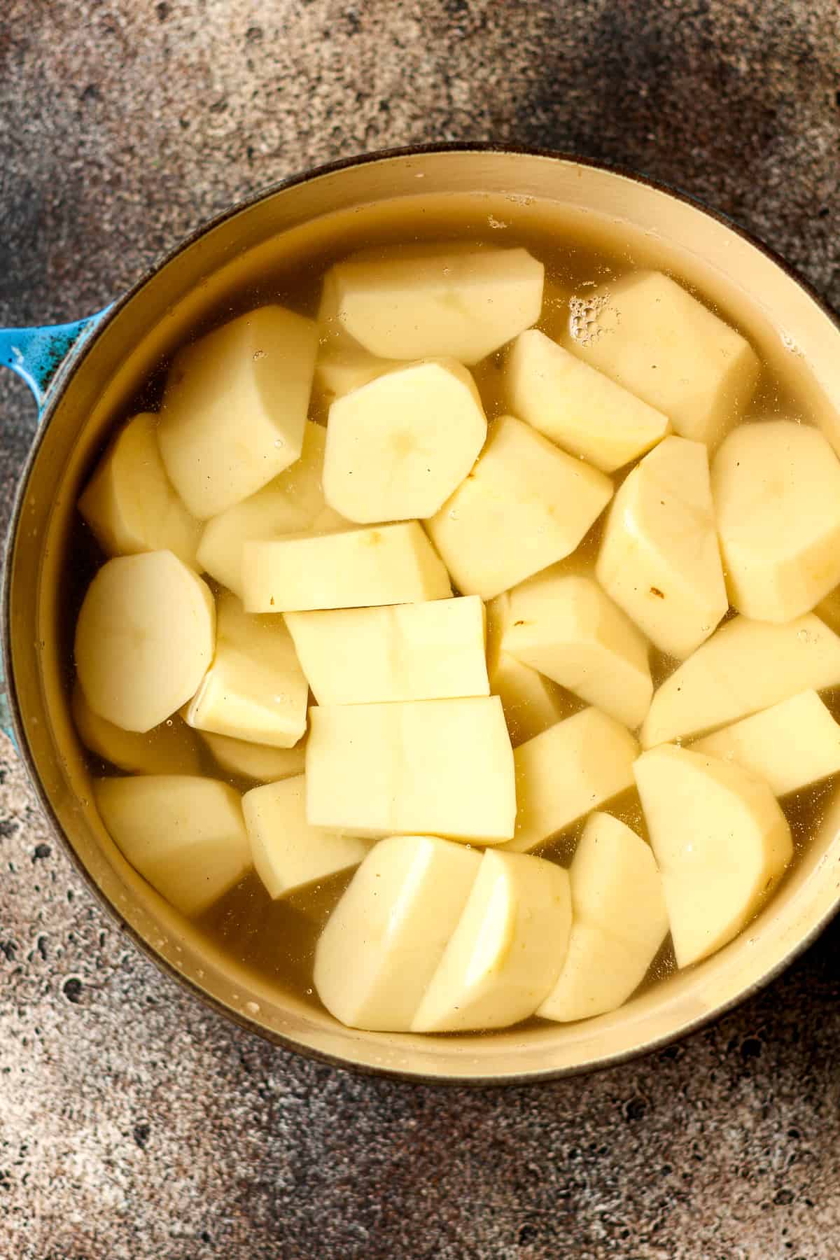 A stock pot of raw chunks of potatoes covered in water.
