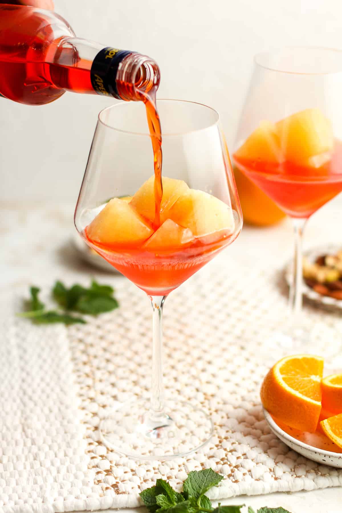 A bottle of aperol being poured into a wine glass with orange ice cubes.