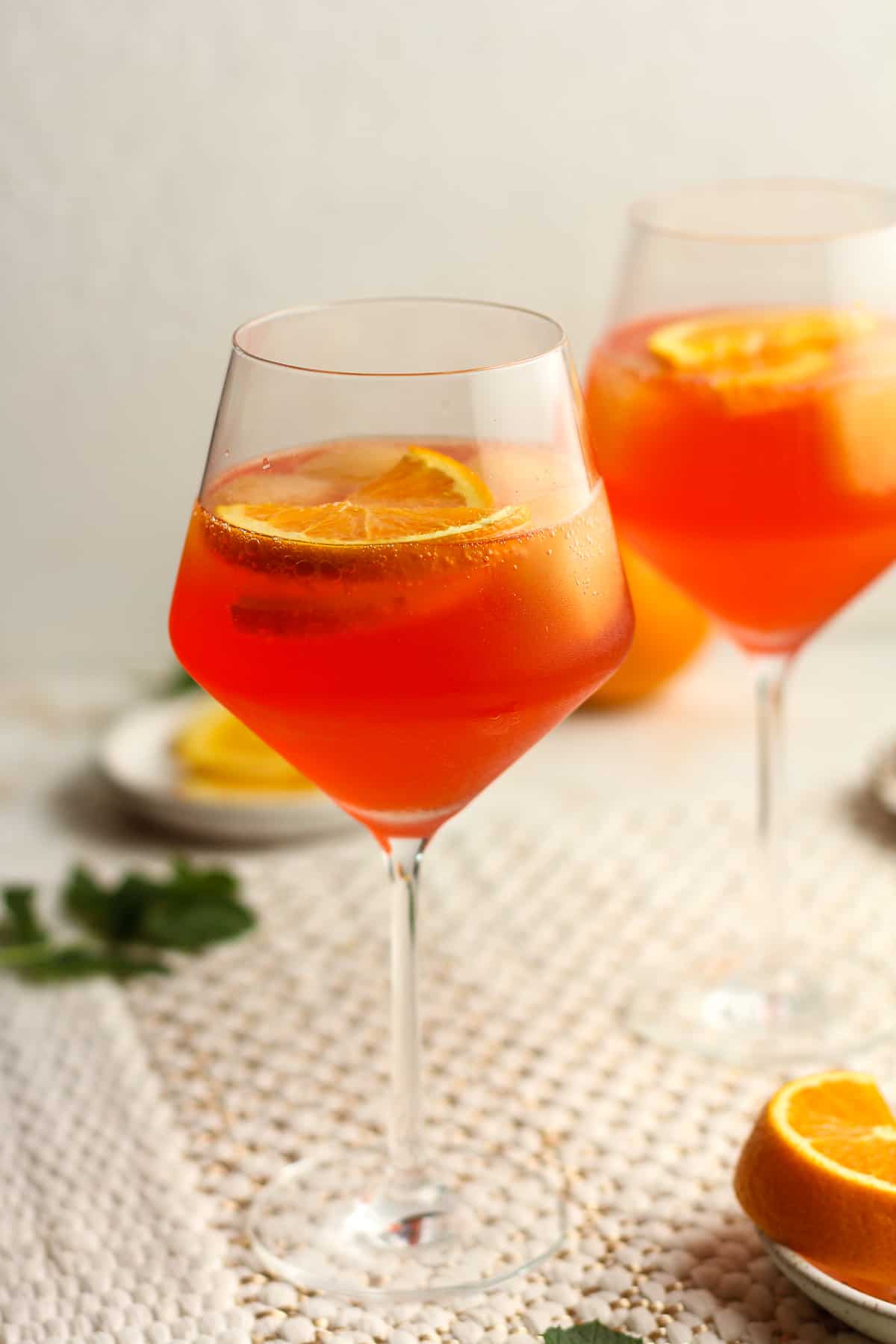 Side view of two glasses of aperol spritz with orange slices.