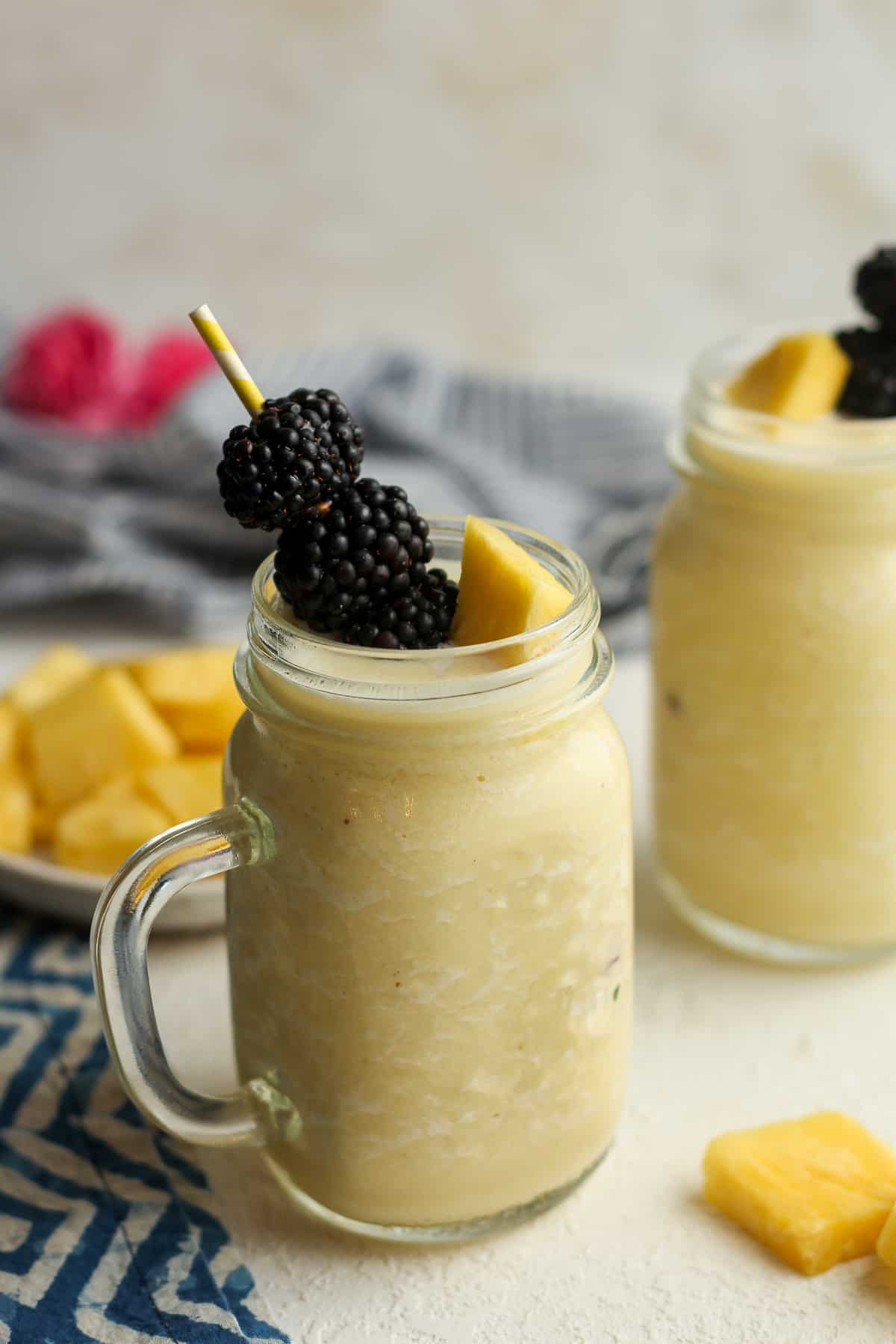 Side shot of two pineapple smoothies with blackberry garnish.