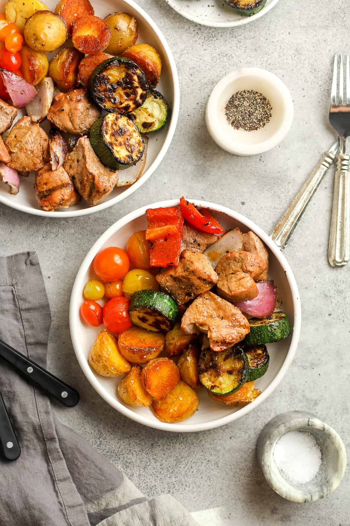 Overhead shot of two bowls of the pork kabobs and veggies on a gray background.