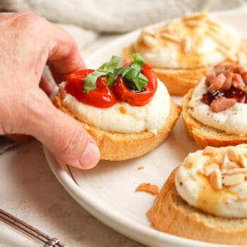 My hand reaching for a ricotta crostini with roasted tomatoes.