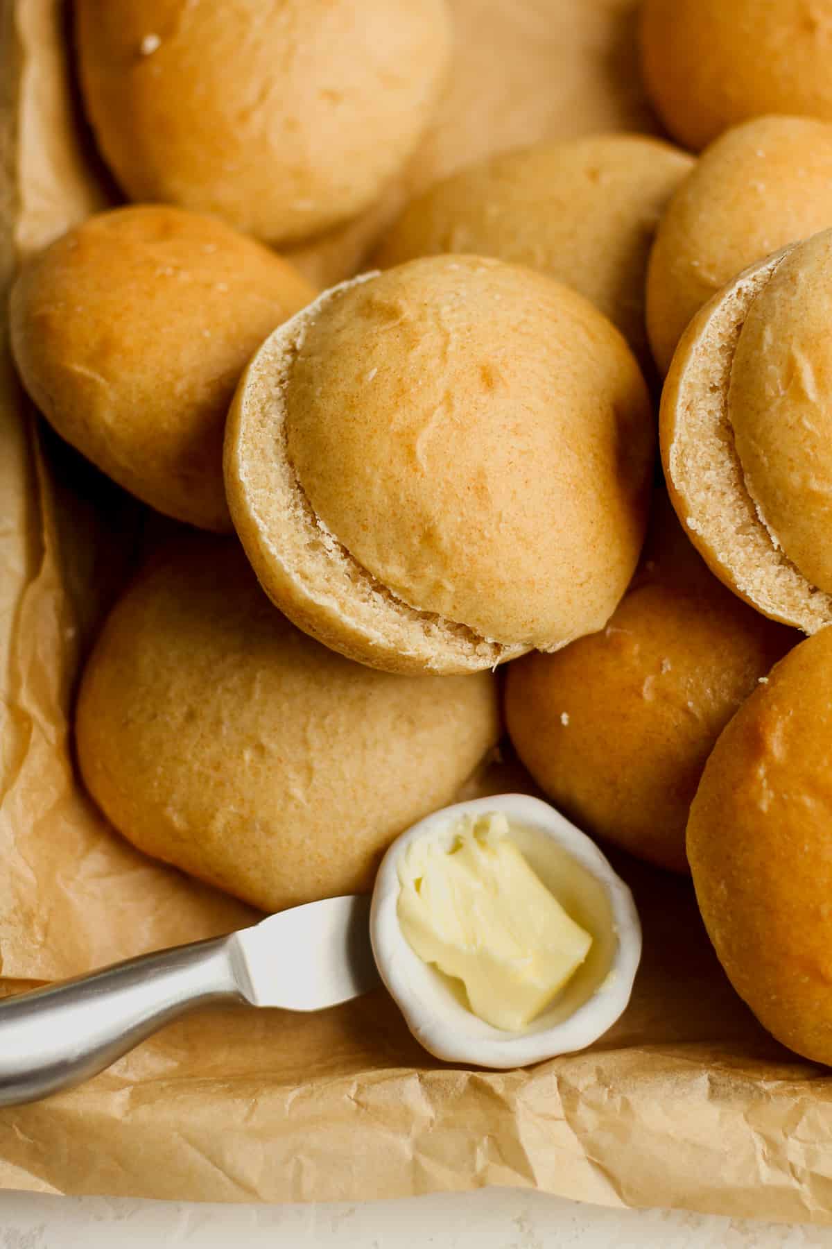A pan of some honey wheat burger buns with a small little bowl of butter.