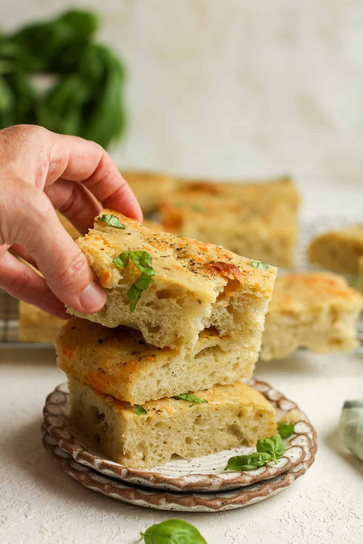 A hand reaching for a piece of sourdough focaccia from a stack.