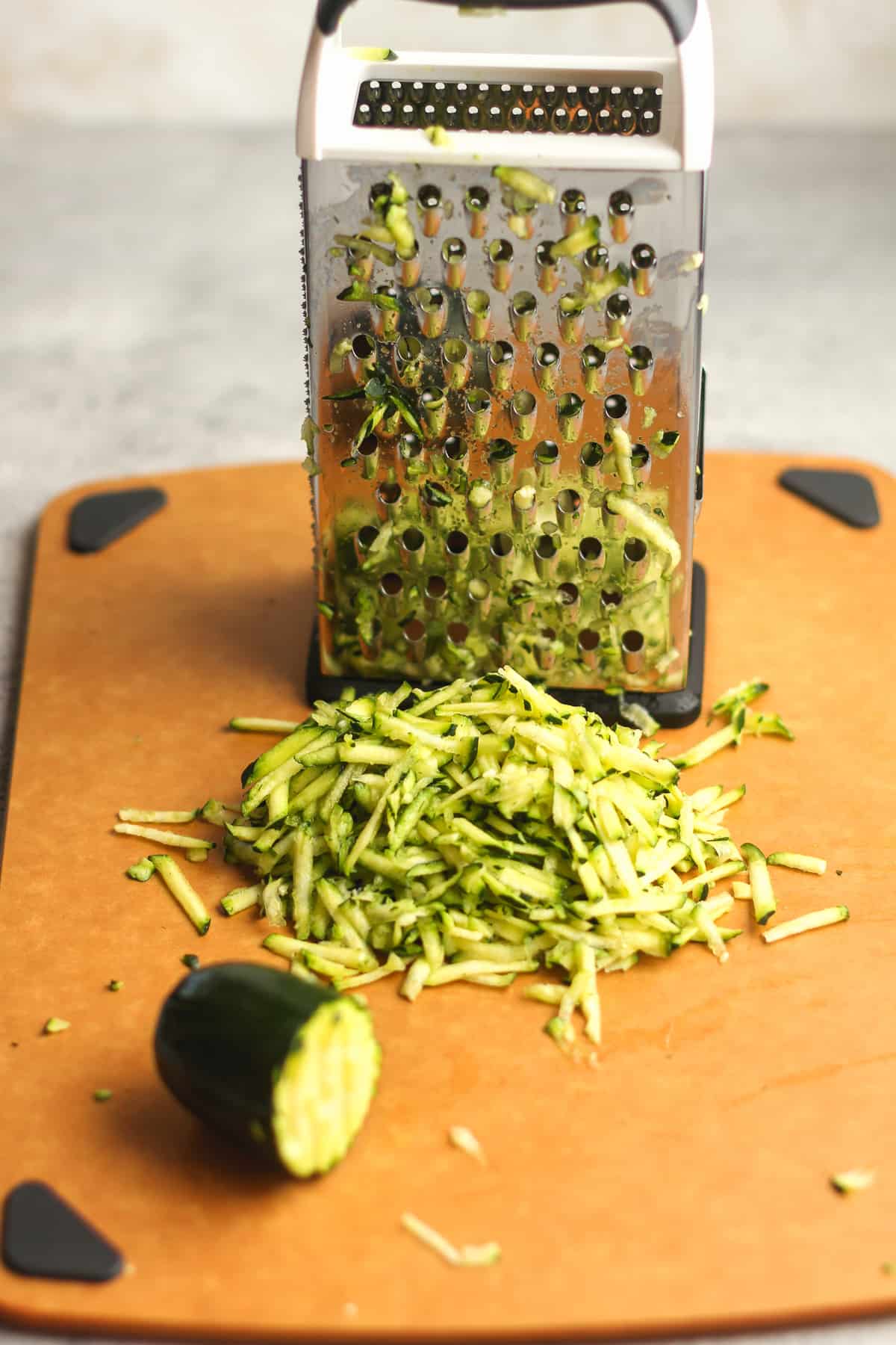 Side view of a board of shredded zucchini next to a box grater.