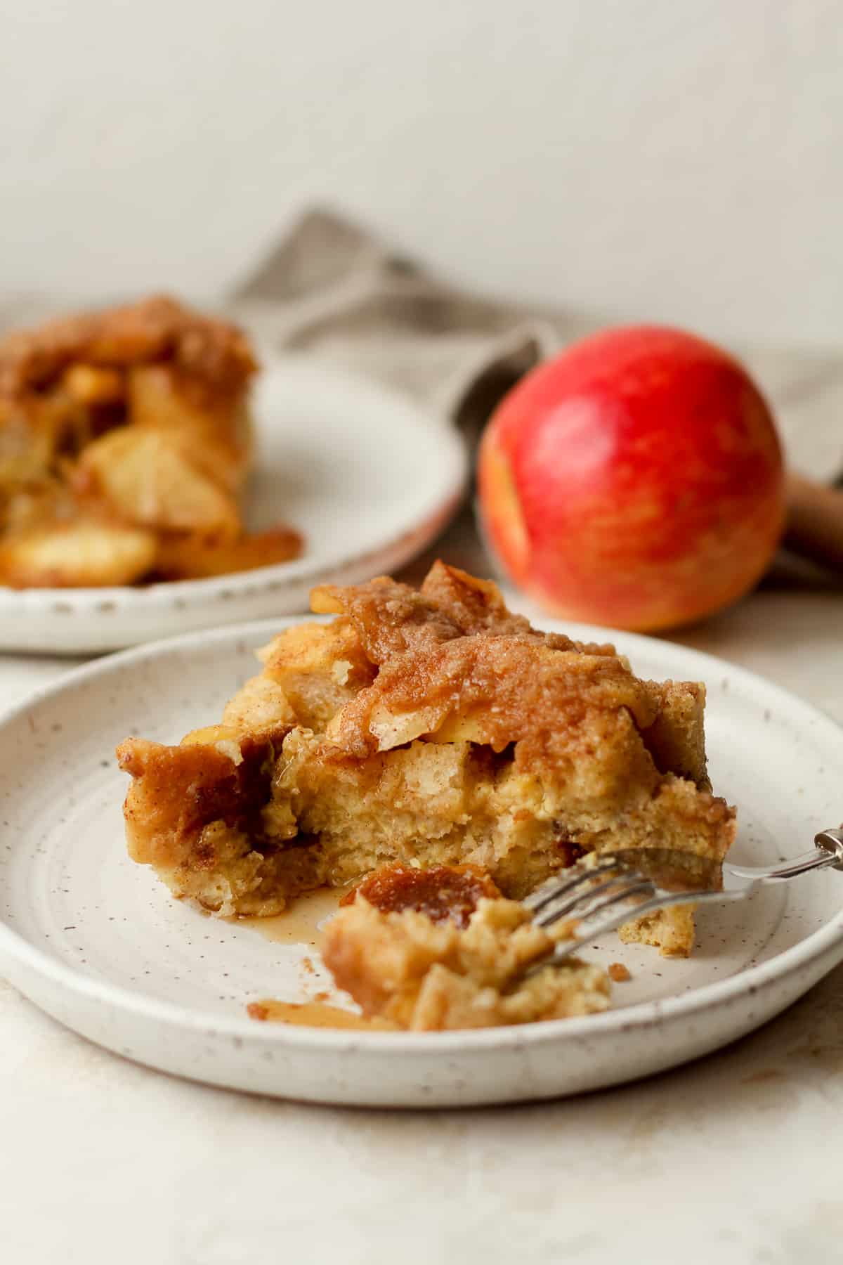 Side view of a slice of cinnamon apple French toast bake with an apple in the background.