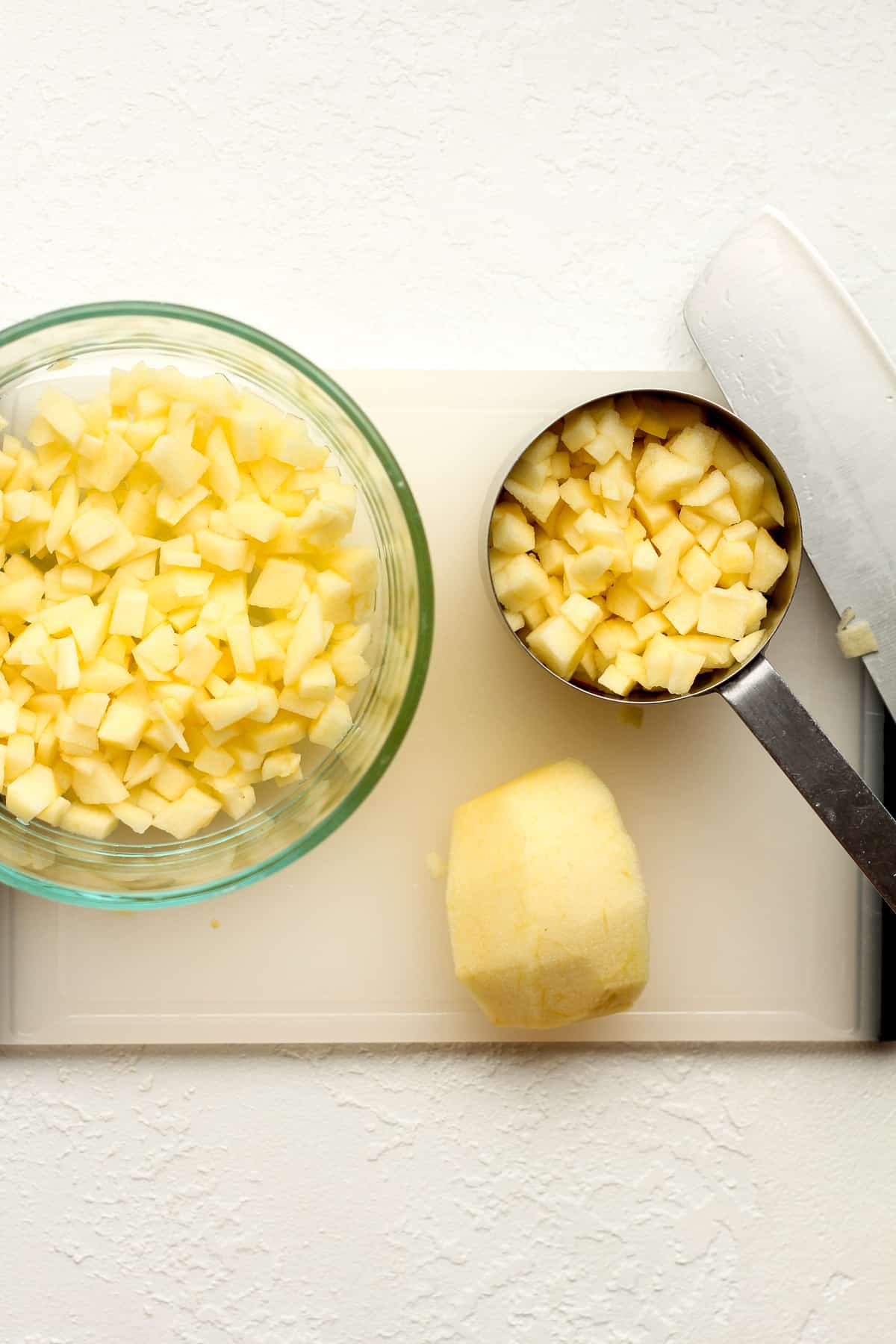 A bowl of diced apples with a knife on a cutting board.