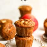 Two stacked apple muffins on a plate with more around it.