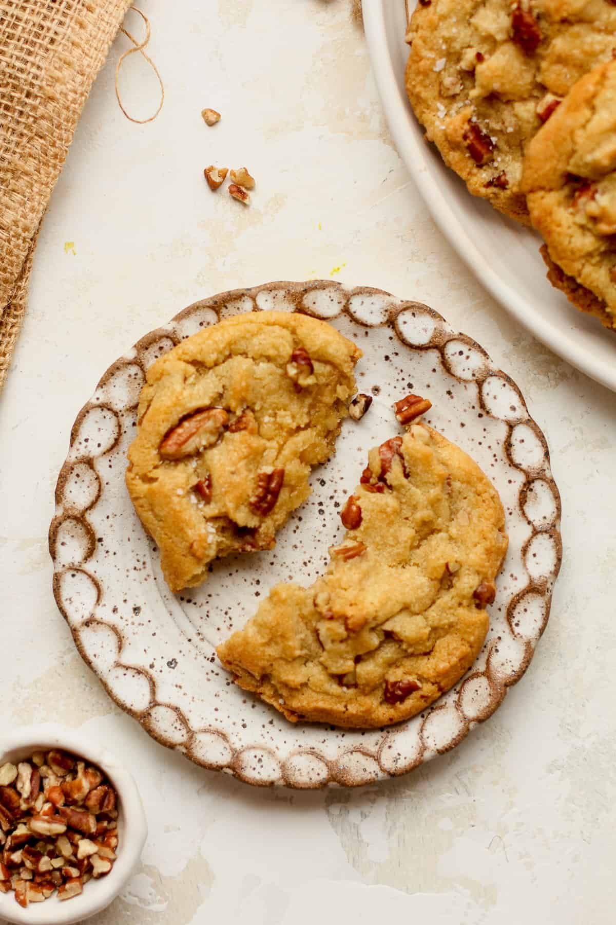 A small plate with a halved brown butter cookie with pecans.