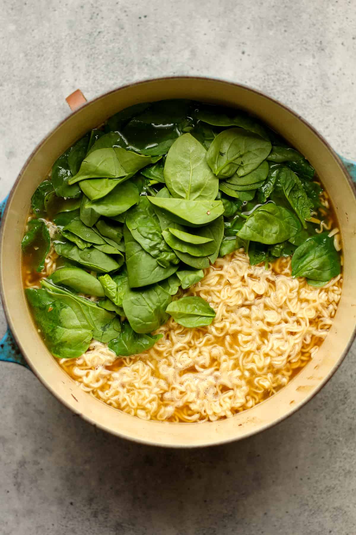 A pot of broth with ramen noodles and baby spinach on top.