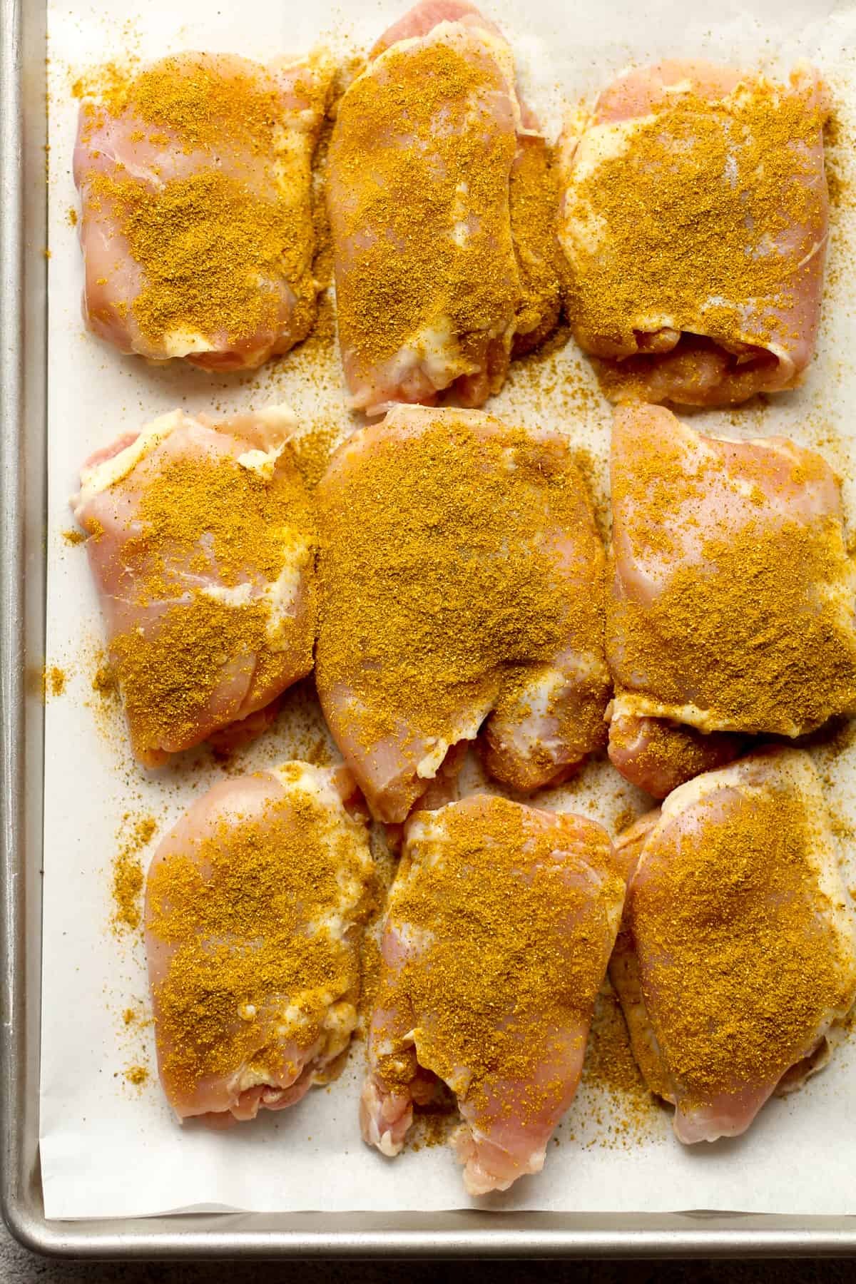 Nine chicken thighs on a baking sheet, with curry powder.