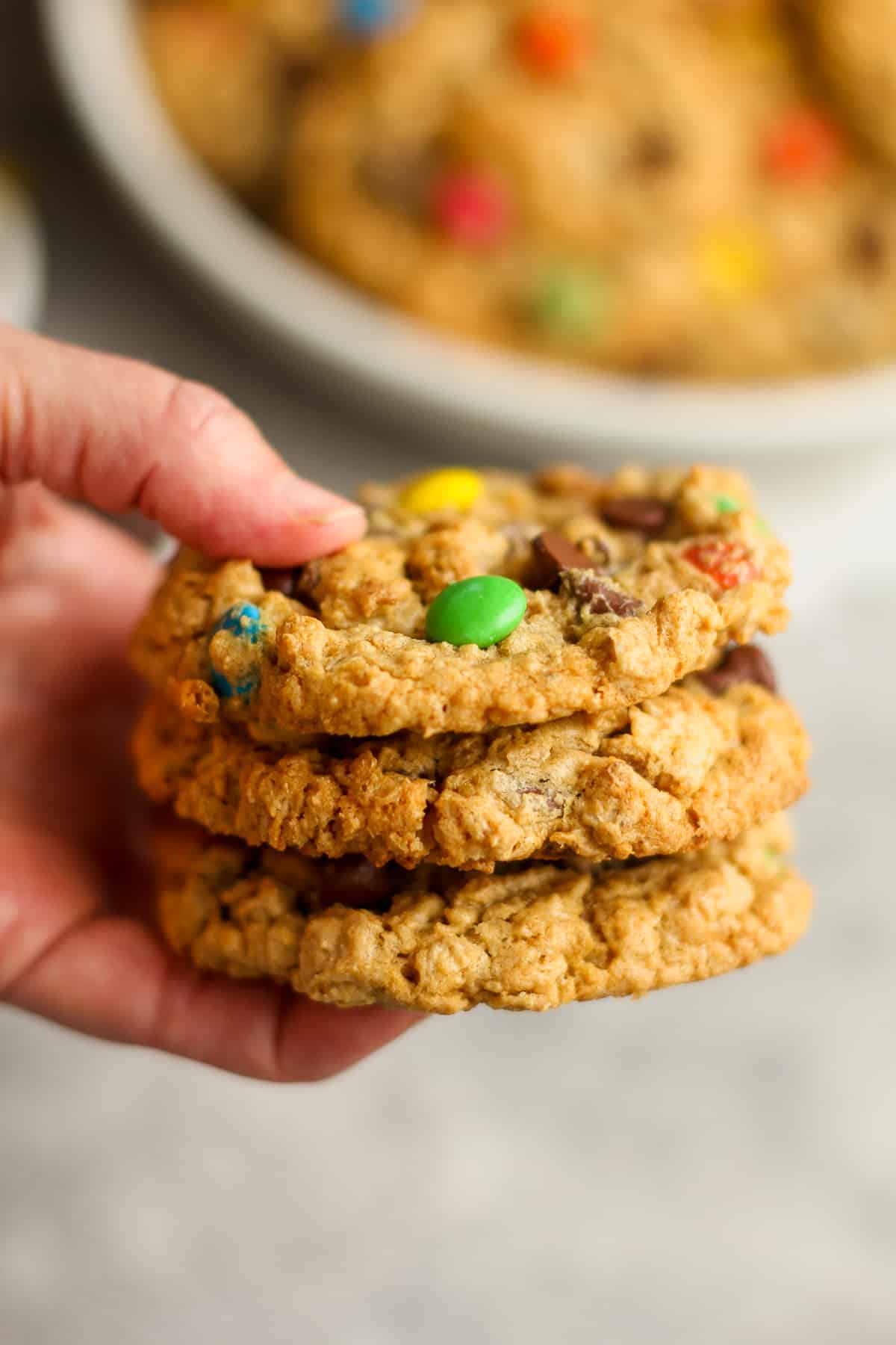 My hand holding three flourless monster cookies with m&ms.